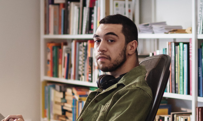 Young man sitting on his wheelchair at a desk with a book shelf behind.