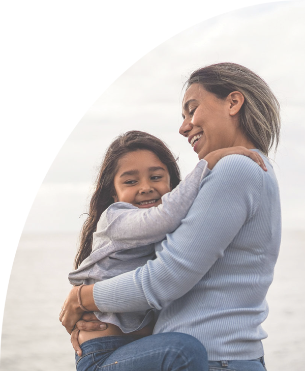 Mum and daughter embrace on a beach.